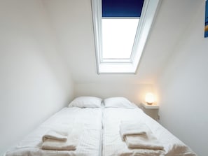 Ein Einzelbett mit weißer Bettwäsche und zwei Handtüchern, eine Nachttischlampe und ein Oberlicht.