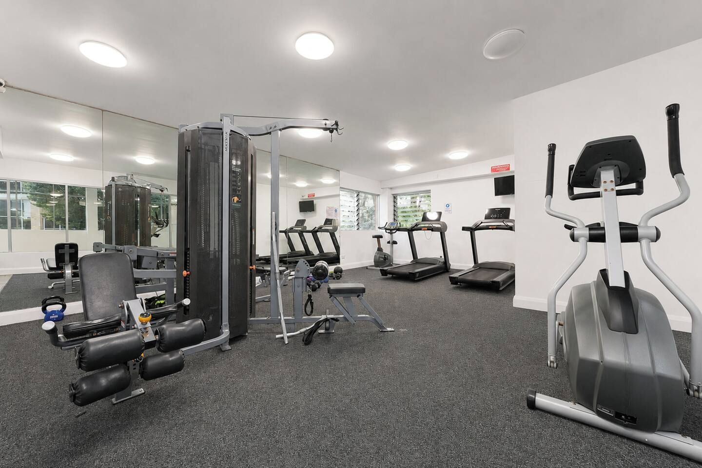 A gym with cardio machines, weightlifting equipment, and a mirrored wall.