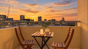 An outdoor balcony with a wooden table and chairs, a candle, and a vase with plants.