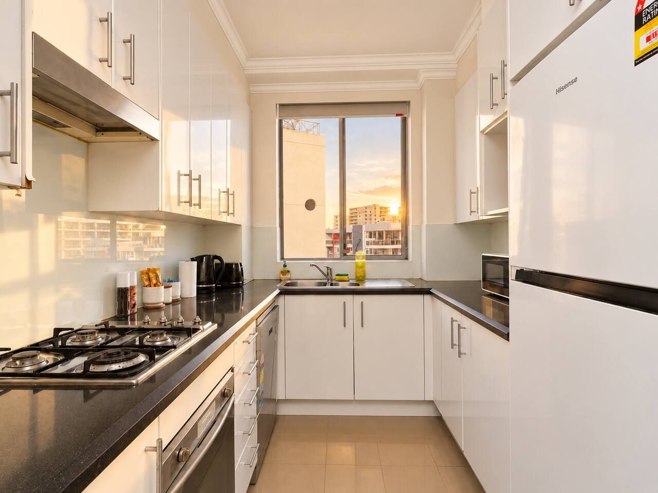 A modern kitchen with white cabinets, a gas stove, and a window with a city view.