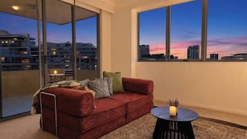 A modern living room with a red sofa, a round black coffee table, and a view of the city skyline at dusk.