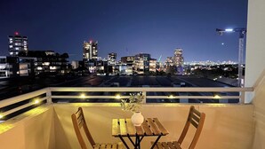 A balcony with a table and chairs, overlooking a cityscape at night. - The Ember | 2BR|2BA|Pool, Gym, Sauna + Parking | Boutique Stay near Sydney CBD (Waterloo)