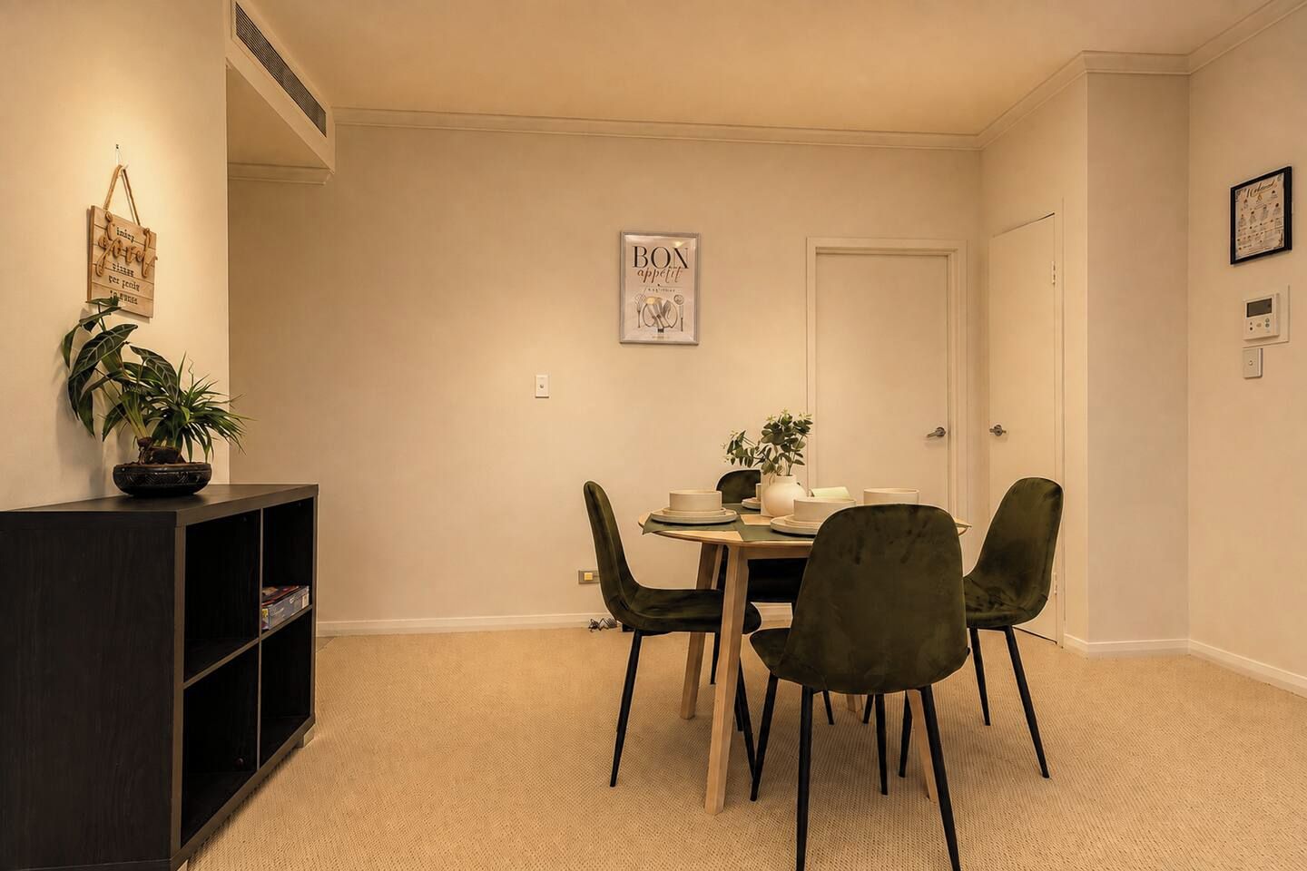 A dining area with a table set for four, surrounded by chairs, a bookshelf, and a potted plant.