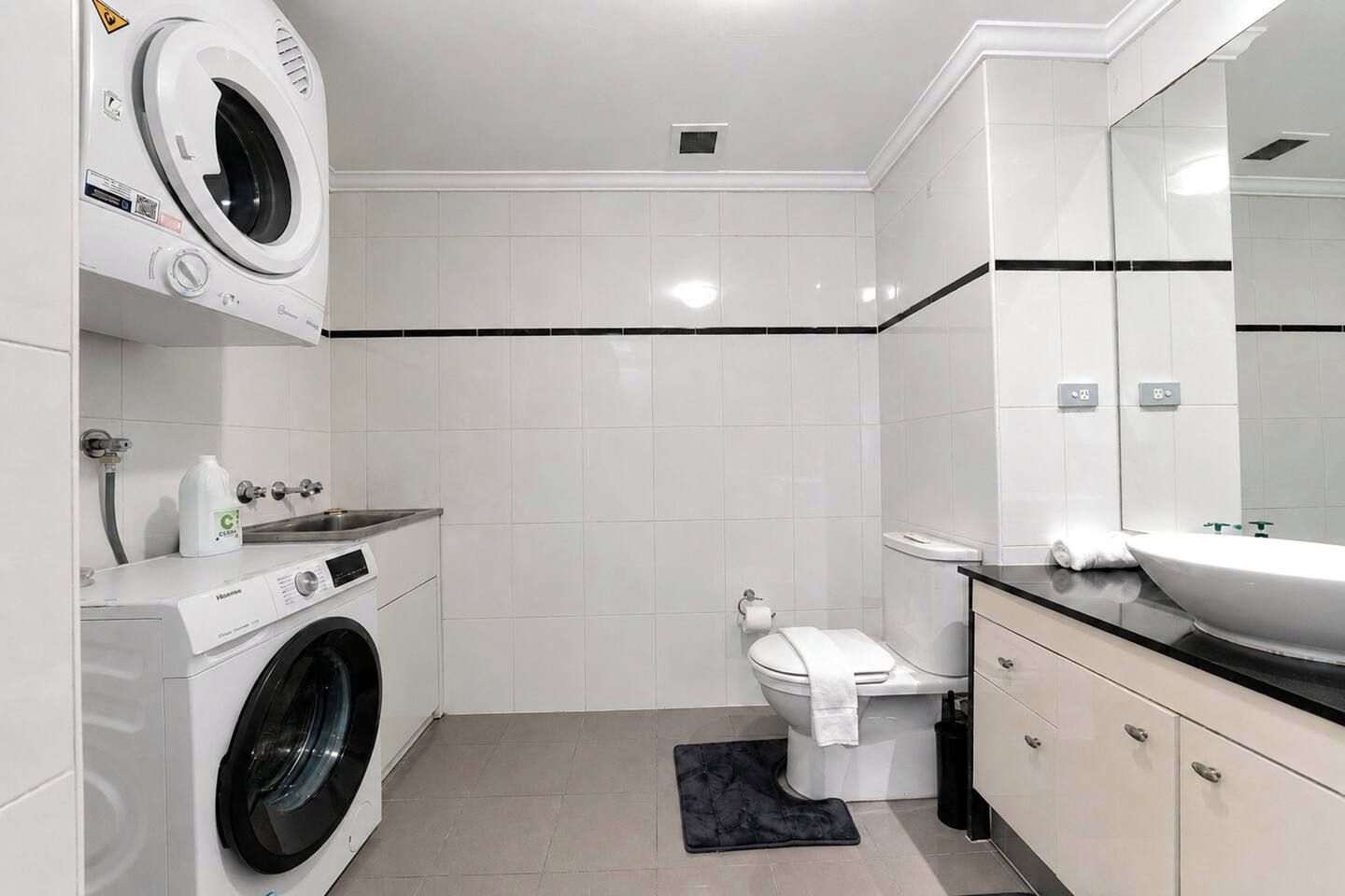A modern bathroom with a washing machine, toilet, sink, and a large mirror.
