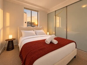 Habitación de hotel con una cama grande, vista de la ciudad a través de una ventana y una puerta corredera.