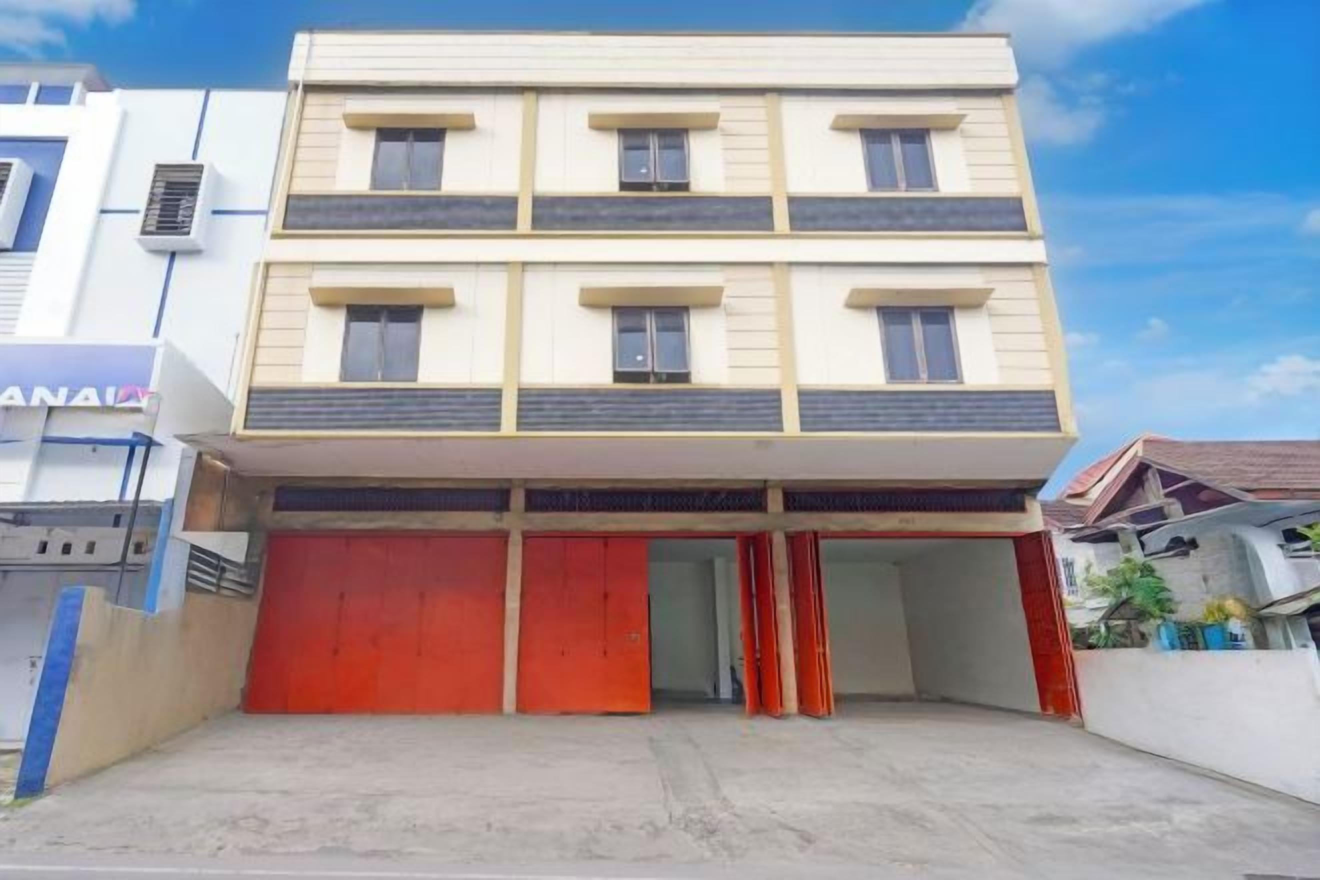 Un edificio de varios pisos con techo plano, puerta de garaje roja y entrada visible.
