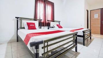 Una cama doble con colcha blanca y roja, dos almohadas, una mesita de noche y una ventana con cortinas.