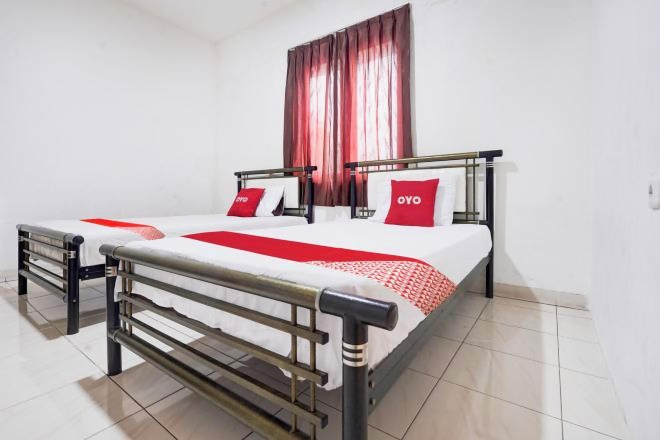 Una cama doble con estructura metálica, dos almohadas y una colcha roja y blanca.