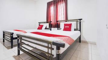 Una cama doble con estructura metálica, dos almohadas y una colcha roja y blanca.