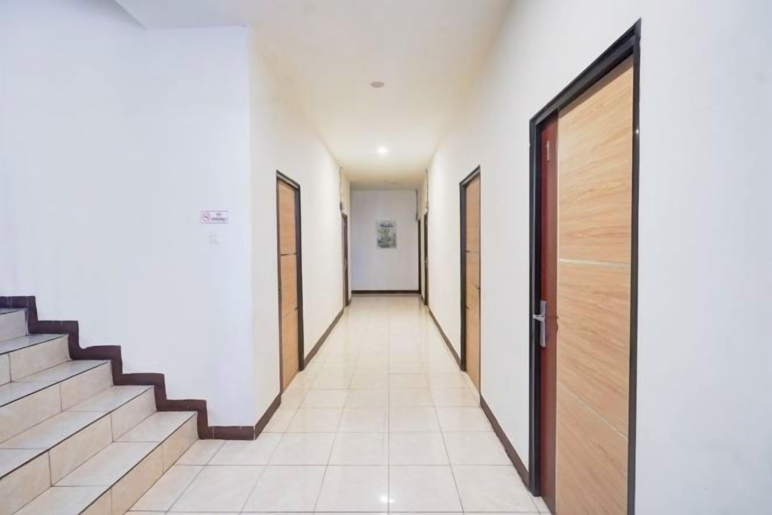 Un pasillo con una escalera a la izquierda, puertas de madera a la derecha y suelo de baldosas.