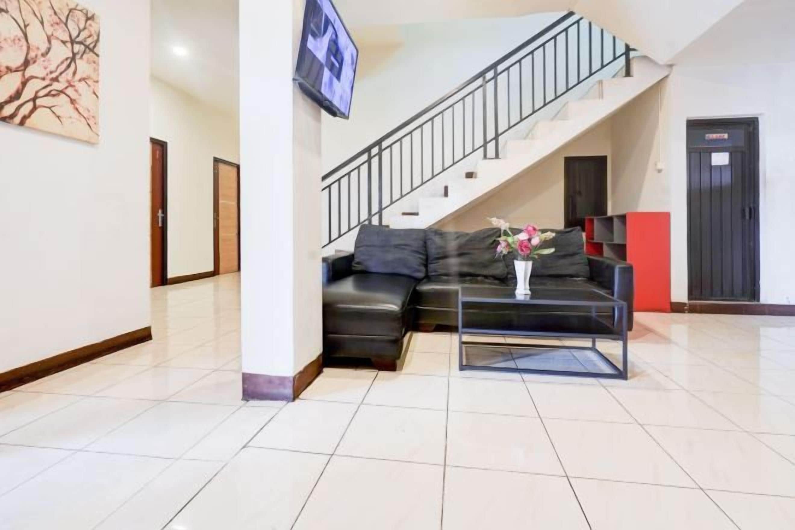 A modern living room with a black leather sofa, a glass coffee table, and a staircase leading to an upper level.