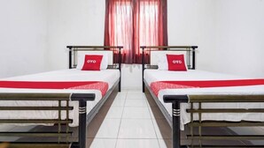 Une chambre avec deux lits simples, chacun agrémenté d’un oreiller rouge et d’une couverture blanche.