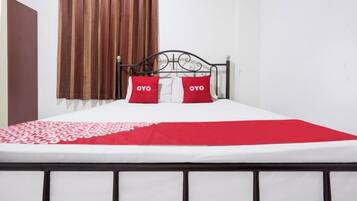 Una cama con estructura metálica, ropa de cama blanca y dos almohadas rojas con el texto 'OYO'.