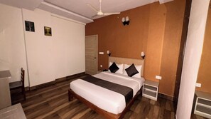 A hotel room with a bed, a ceiling fan, a door, and a small table.