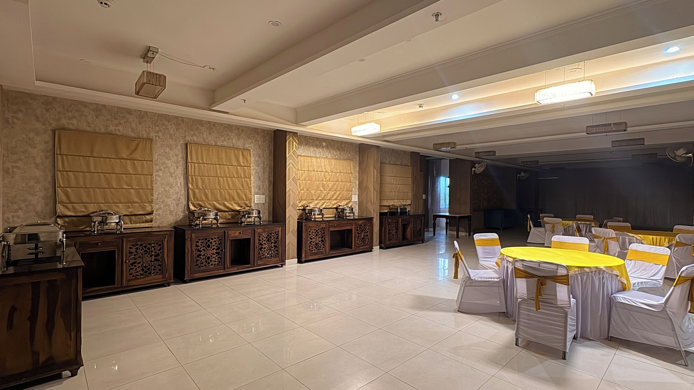 A banquet hall with a stage, tables with white and yellow tablecloths, and a tiled floor.