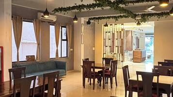 A dining area with wooden tables and chairs, hanging pendant lights, and a view into the kitchen area.