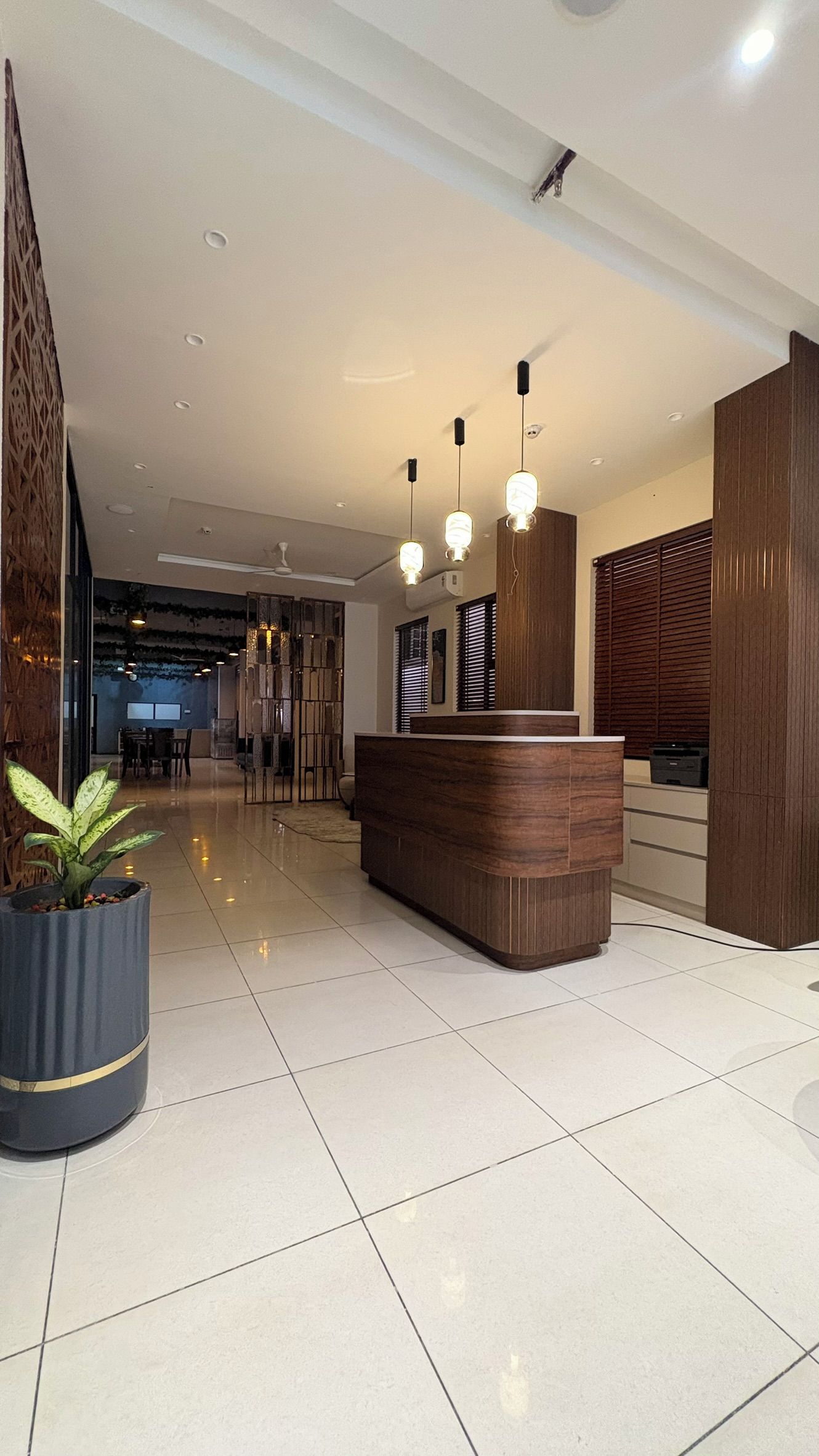 A reception area with a wooden reception desk, a potted plant, and a modern ceiling design.