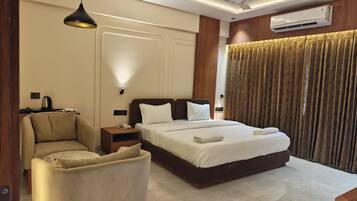 A hotel room with a bed, a chair, a bedside table with a lamp, an air conditioning unit, and a ceiling fan.