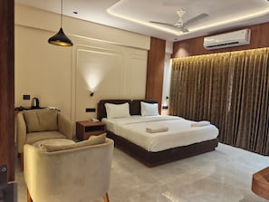 Ein Hotelzimmer mit einem Bett, einem Sessel, einem Nachttisch mit Lampe, einer Klimaanlage und einem Deckenventilator.