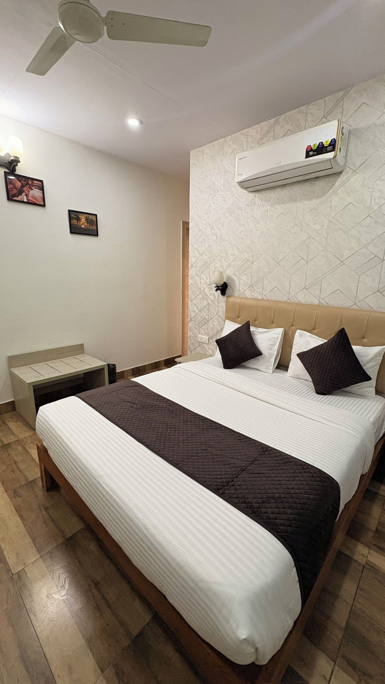 Habitación de hotel con cama, mesita de noche, ventilador de techo y aire acondicionado instalado en la pared.