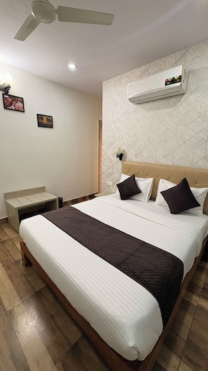 A hotel room with a bed, a bedside table, a ceiling fan, and a wall-mounted air conditioner.