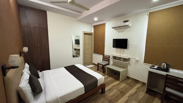 A hotel room with a bed, a desk, a chair, a television, and an air conditioning unit.