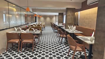 A restaurant with a black and white checkered floor, multiple tables with white napkins, and orange pendant lighting.