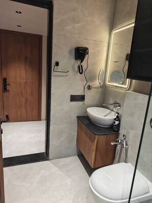 Ein modernes Badezimmer mit Toilette, Waschbecken und Dusche. Ein Föhn ist an der Wand montiert und über dem Waschbecken befindet sich ein Spiegel.