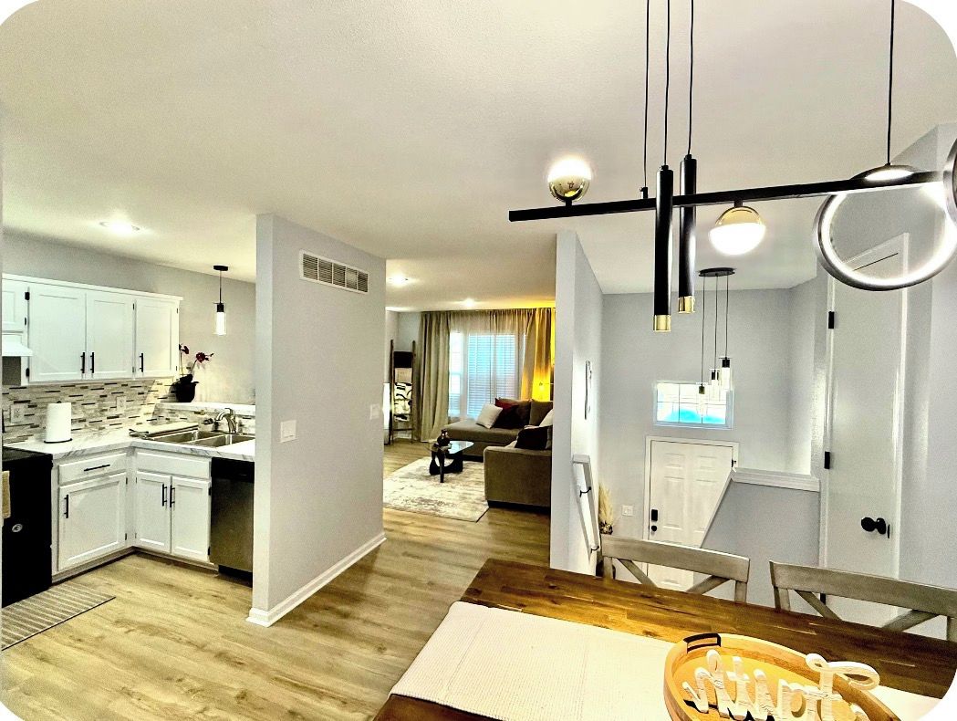 Une cuisine moderne avec des meubles blancs, un coin repas doté d’une table en bois et un salon avec un canapé et une table basse.