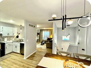 Een moderne keuken met witte kastjes, een eethoek met een houten tafel en een woonkamer met een bank en salontafel.
