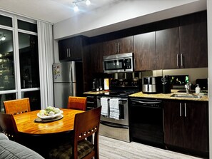 A modern kitchen with dark wood cabinets, stainless steel appliances, and a dining area with a wooden table and chairs. - Condo downtown toronto near Scotiabank arena (Toronto)
