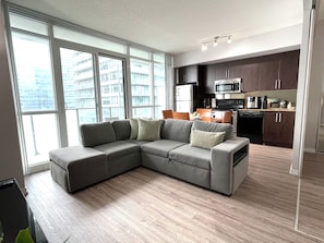A modern living room with a sectional sofa, a dining area, and a kitchen with dark cabinets and stainless steel appliances. - Condo downtown toronto near Scotiabank arena (Toronto)