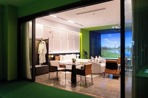A hotel room with a dining area, a sofa set, a large window with a view, and a robe hanging on a door. - Sakki Golf Resort (Shenzhen)