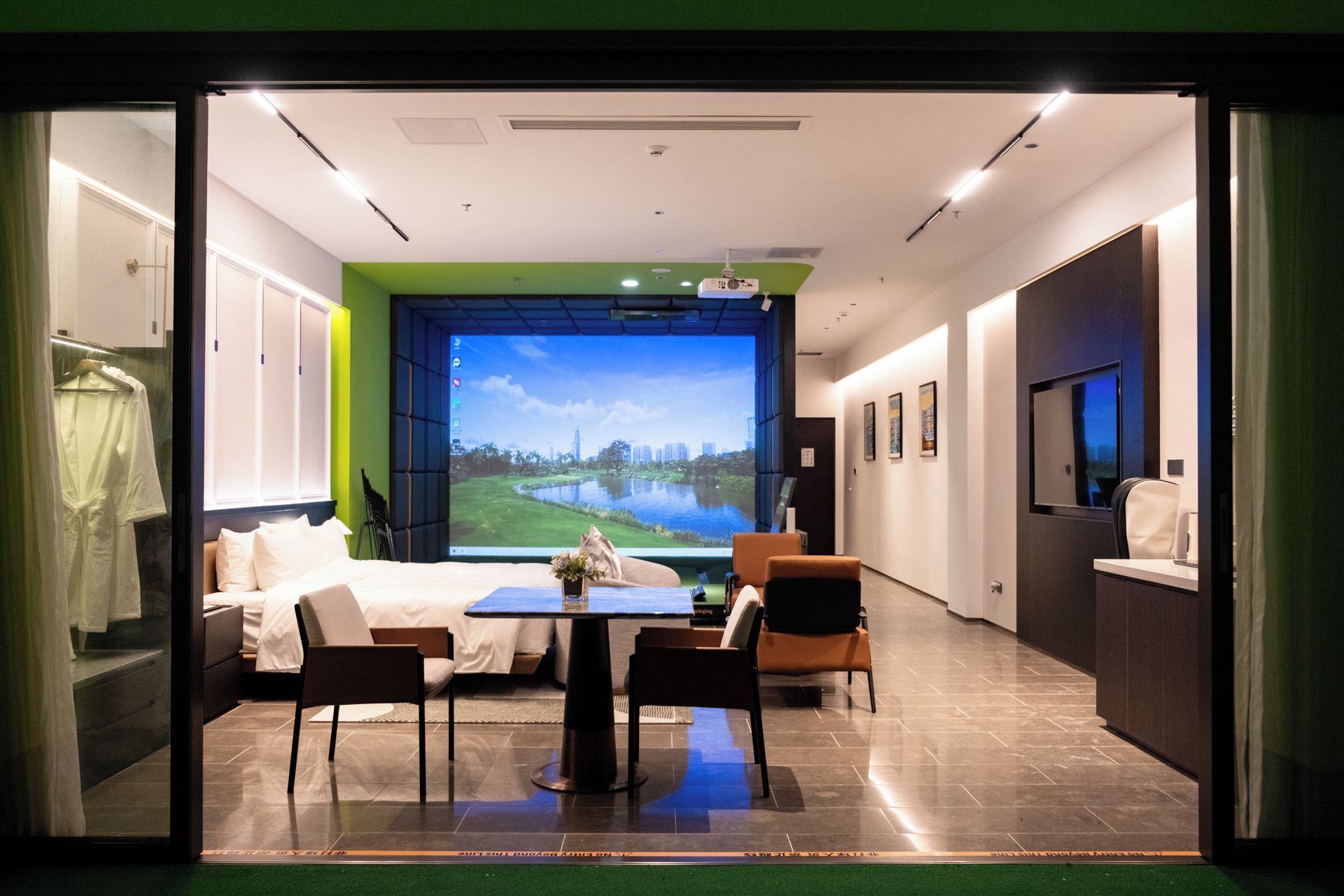 Habitación de hotel con cama, mesa de comedor, sillas, televisor y un amplio ventanal con vistas panorámicas.