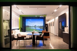 Habitación de hotel con cama, mesa de comedor, sillas, televisor y un amplio ventanal con vistas panorámicas.