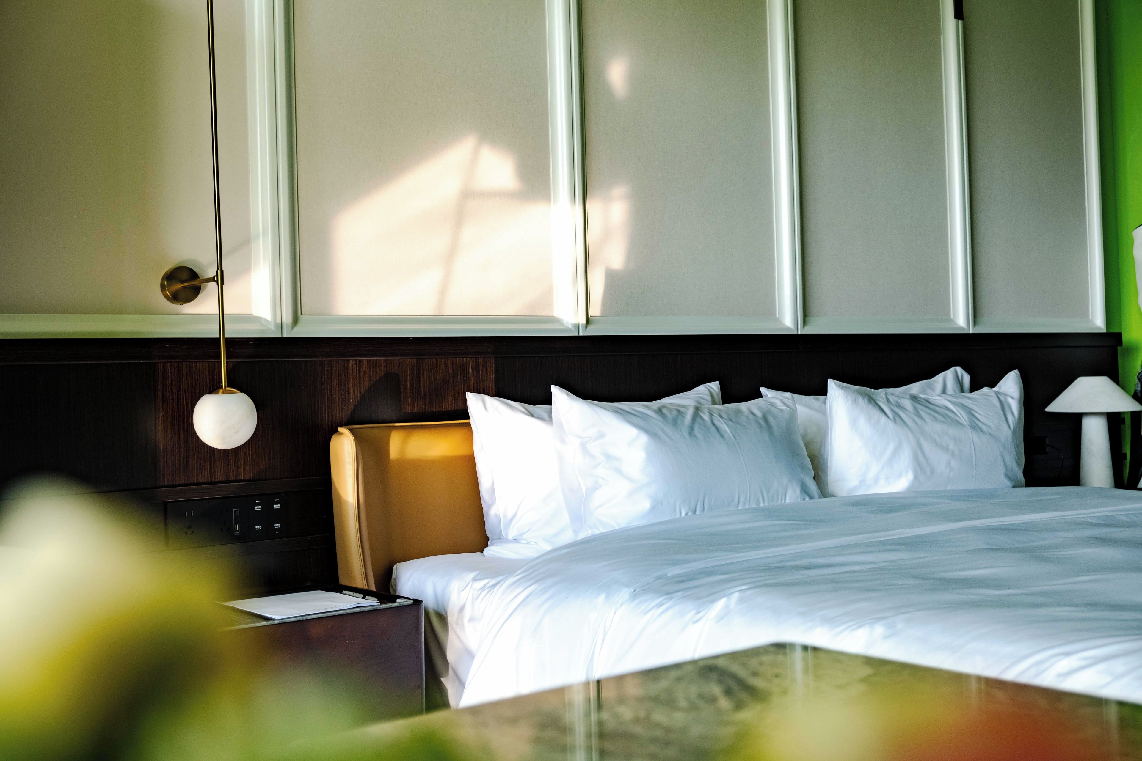 Una habitación de hotel con cama, mesita de noche, lámpara y panel de control en la pared.