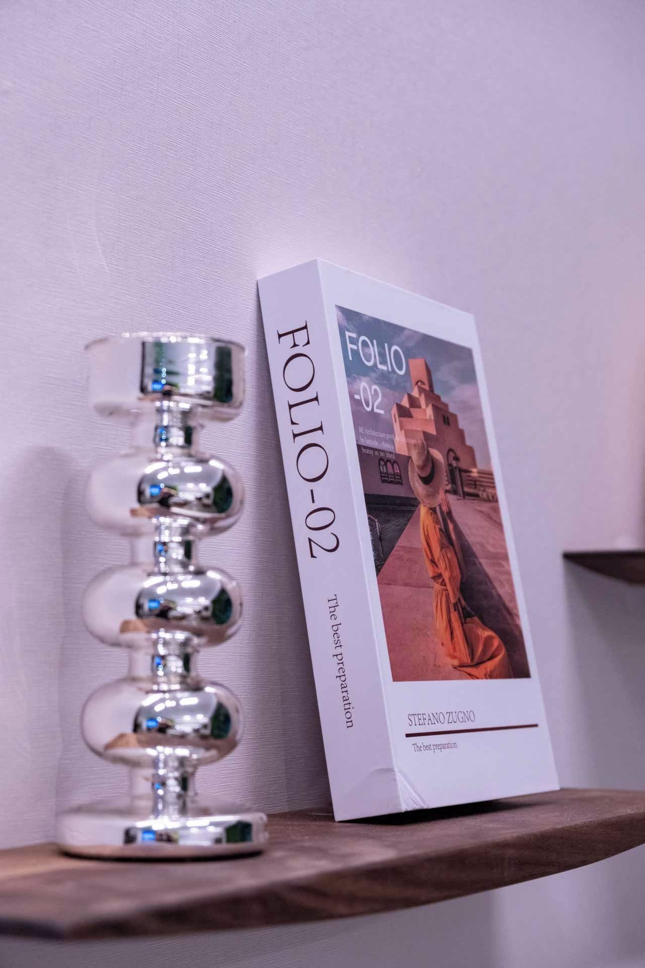 A book titled 'FOLIO -02' by Stefano Zugno on a shelf next to a metallic object.