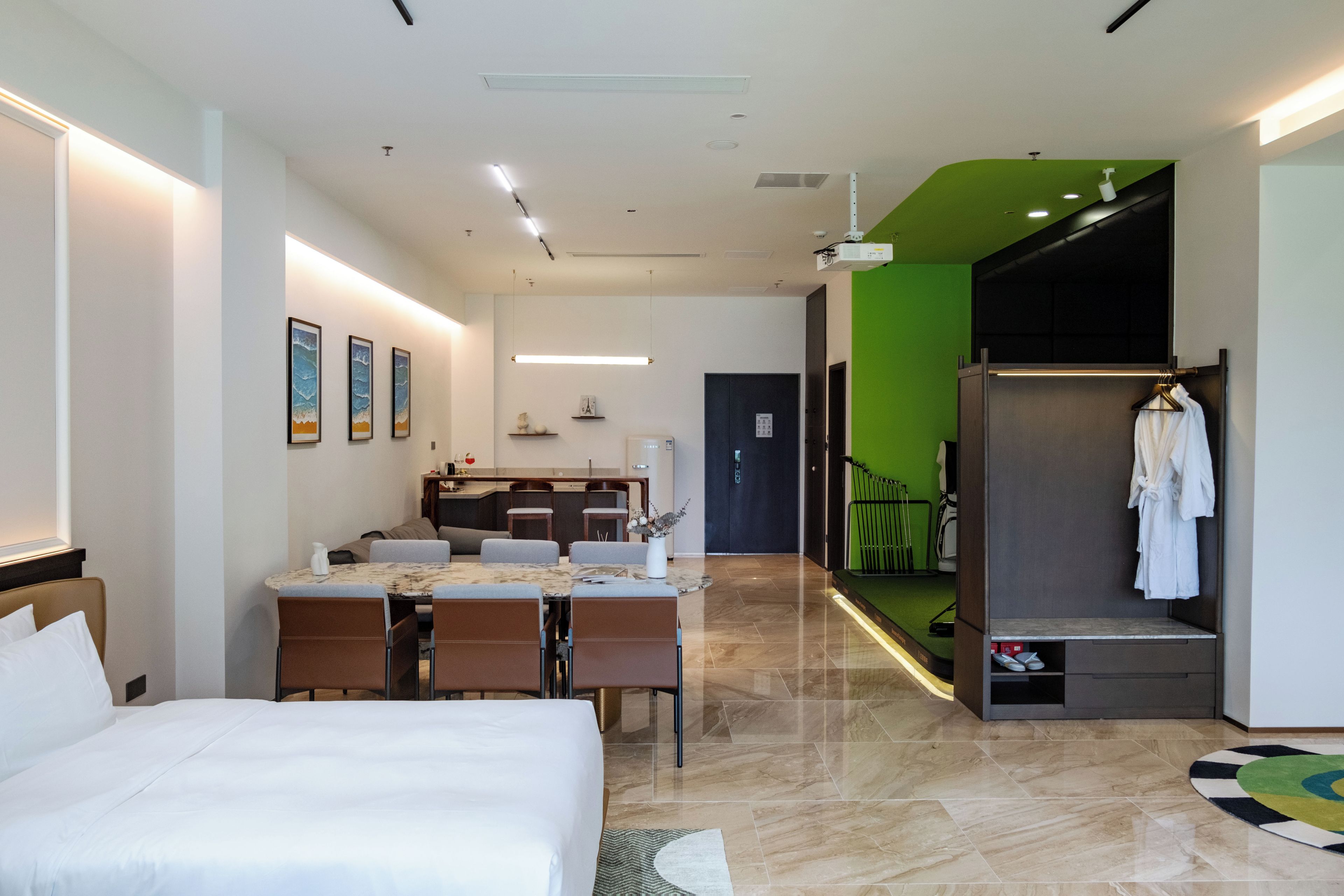 Una habitación de hotel con cama, una mesa de comedor, sillas, kitchenette y una pared de acento verde.