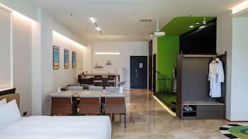 Una habitación de hotel con cama, una mesa de comedor, sillas, kitchenette y una pared de acento verde.