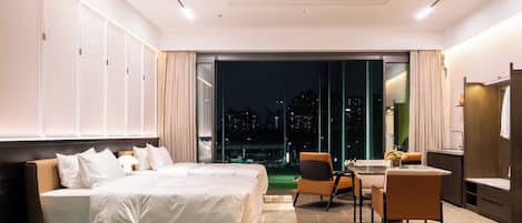 Una habitación de hotel moderna con una cama grande, un espacio para comer y vistas a la ciudad.