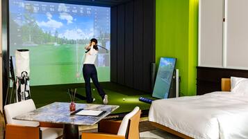 Habitación con una pantalla grande que muestra una simulación de golf, una cama, un escritorio con ordenador y una silla.
