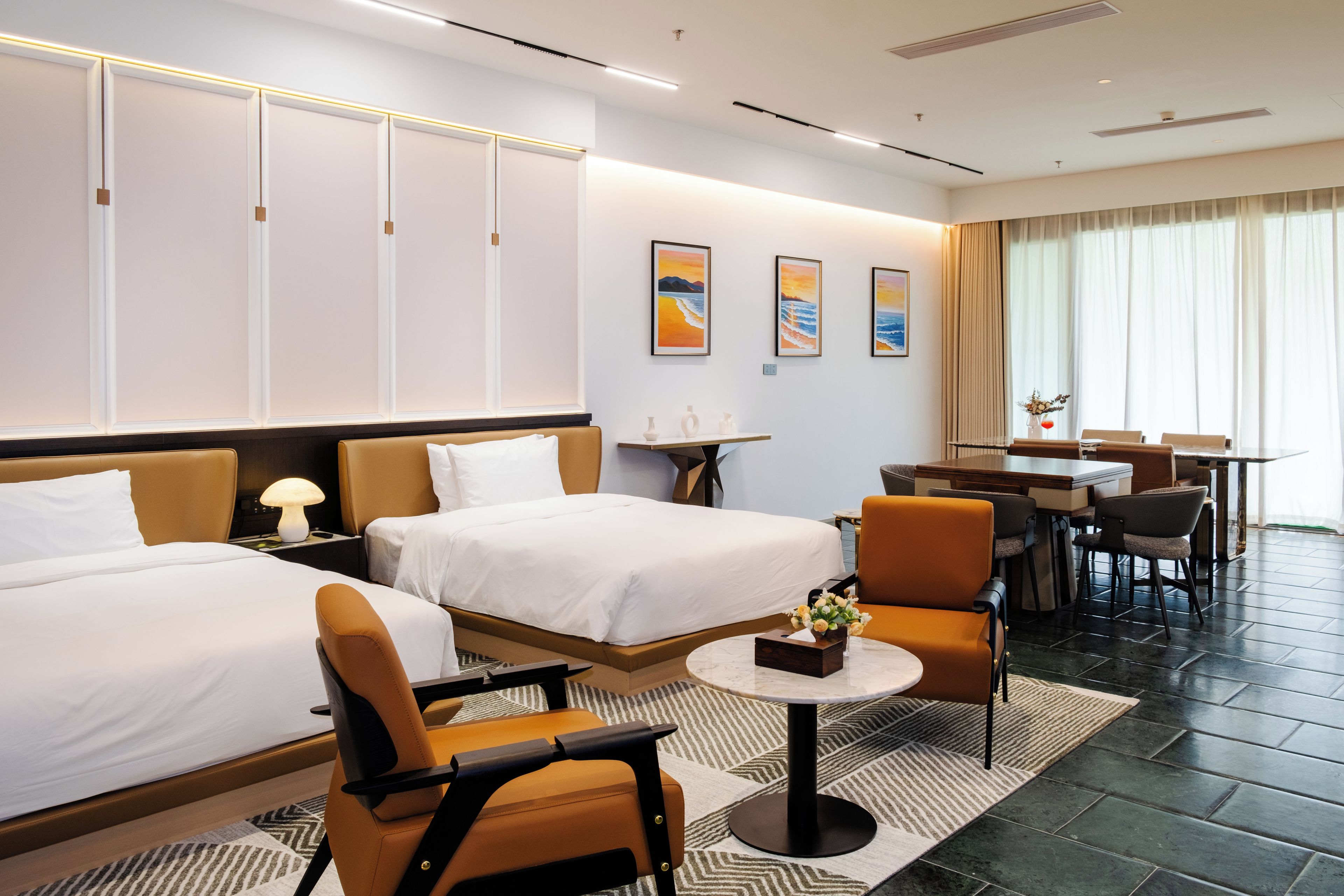 Una habitación de hotel con dos camas, una zona de comedor y obras de arte en las paredes.