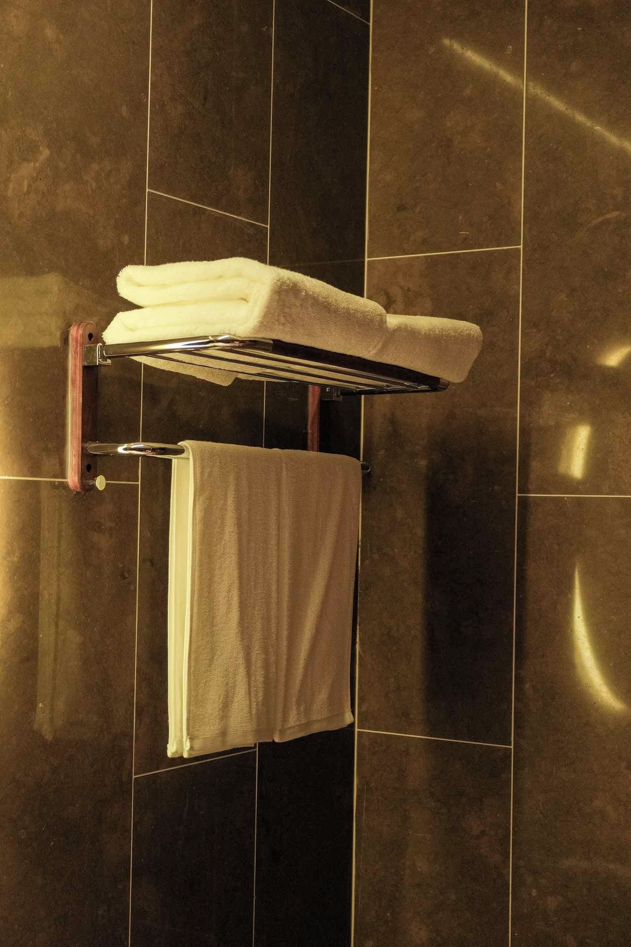 Un bagno con un portascopevoli che contiene un asciugamano piegato e un altro appeso, su uno sfondo di piastrelle.