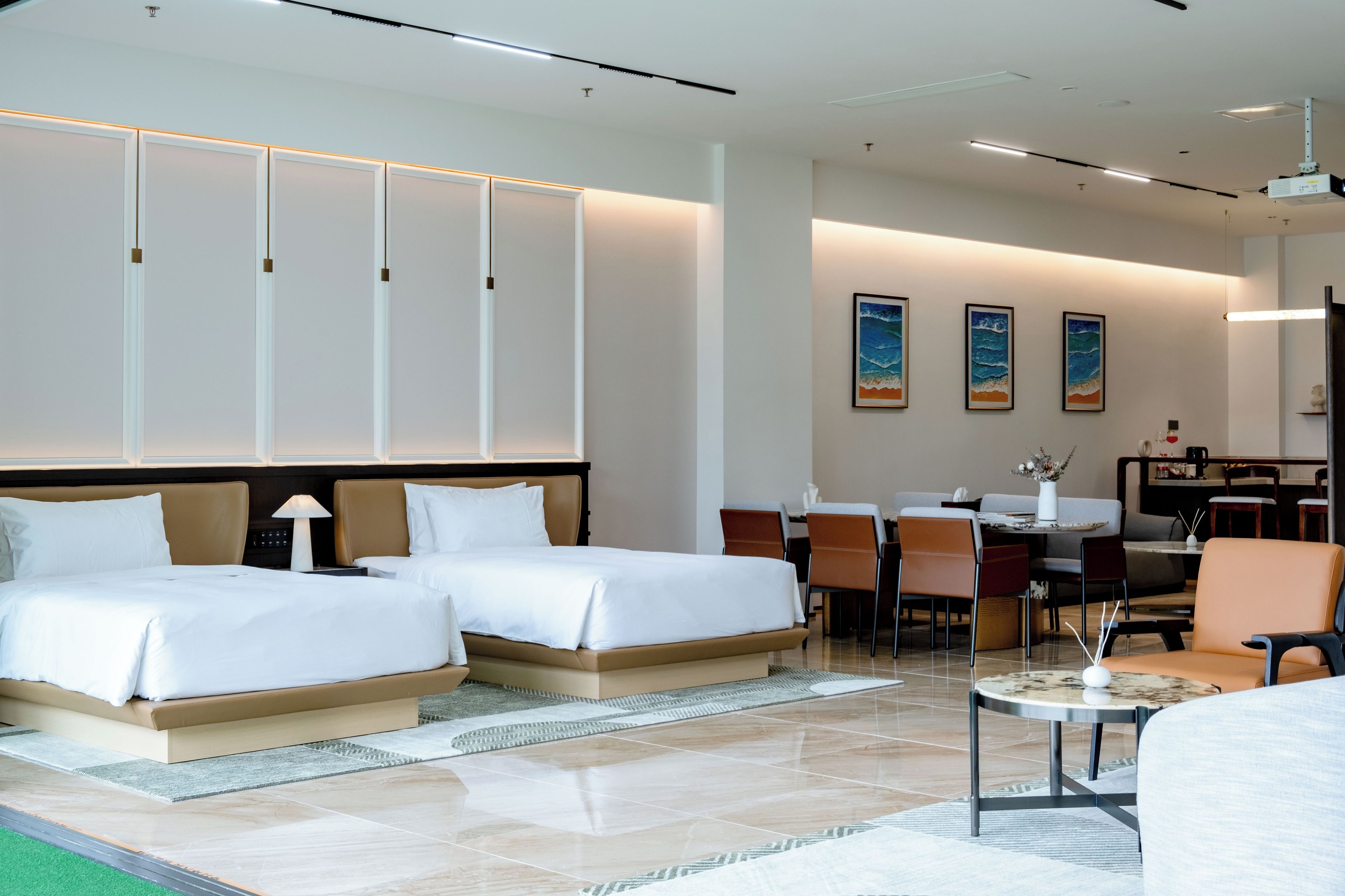 Quarto de hotel com duas camas, área de refeições e sala de estar com cadeiras e mesa.