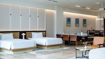 Quarto de hotel com duas camas, área de refeições e sala de estar com cadeiras e mesa.