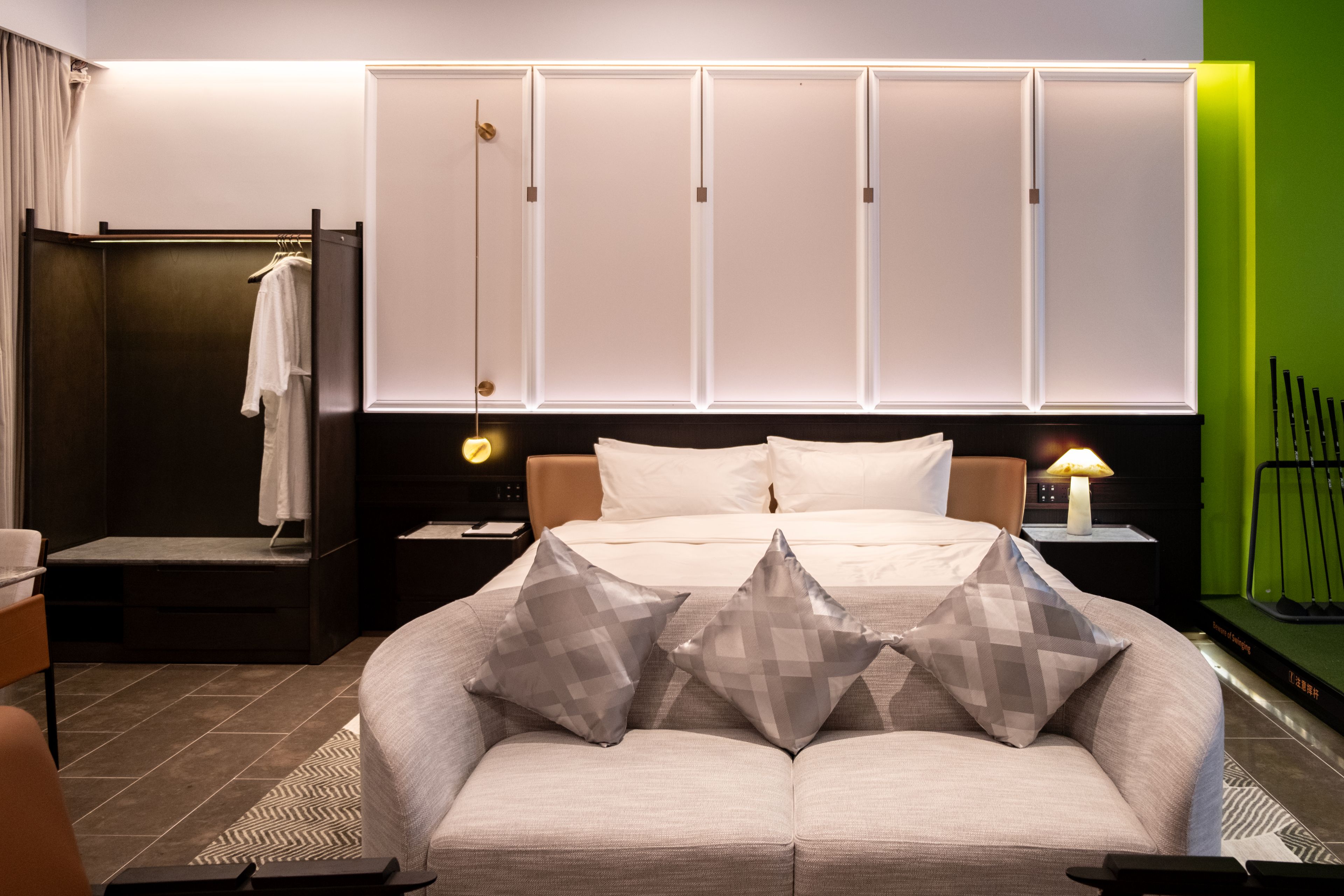 Een hotelkamer met een bed, een slaapbank, een nachtkastje, een lamp en een groene wand.