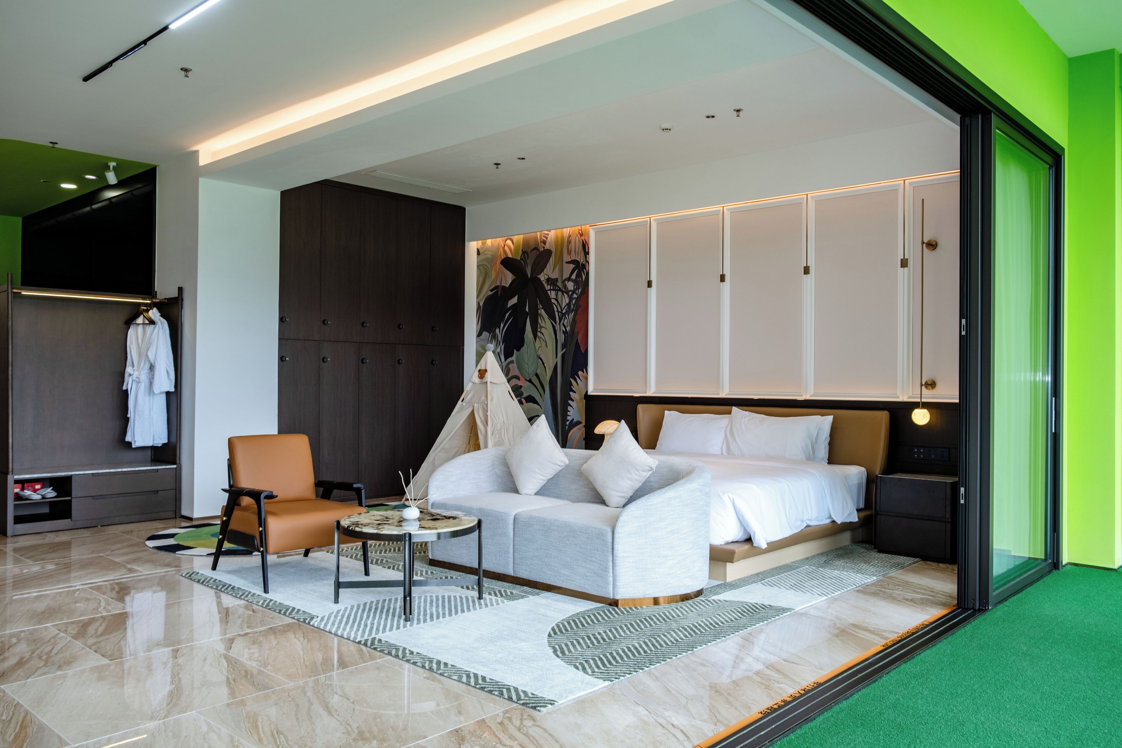 A modern hotel room with a bed, a seating area, and a wardrobe.