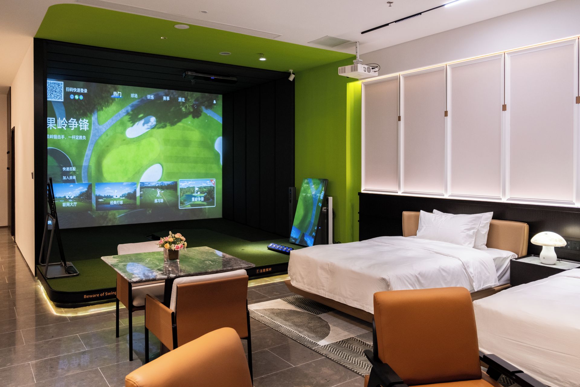Une chambre d’hôtel avec un lit, un bureau avec un ordinateur portable, un écran de projection diffusant un match de golf et une petite table sur laquelle est posé un vase de fleurs.