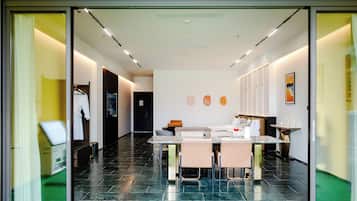 A modern hotel room with a dining area, a bed, and a bathroom visible through the glass door.