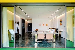 Habitación de hotel moderna con comedor, cama y baño visible a través de la puerta de vidrio.